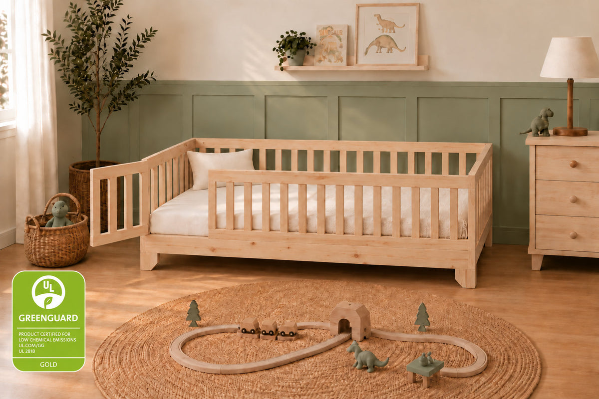A light natural wood daybed with safety rails in a styled children's bedroom. The room features a green paneled lower wall, a wooden dresser, a potted plant, and a round jute rug with a toy train track.