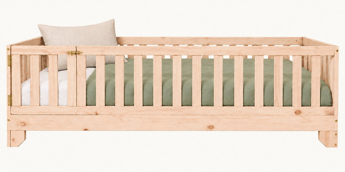A light natural wood toddler bed crib with vertical guard rails and gate.