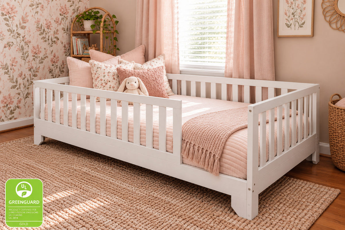 White wooden twin XL size floor bed for toddlers with safety rails in a styled nursery setting, featuring pink bedding, floral wallpaper, and a window.