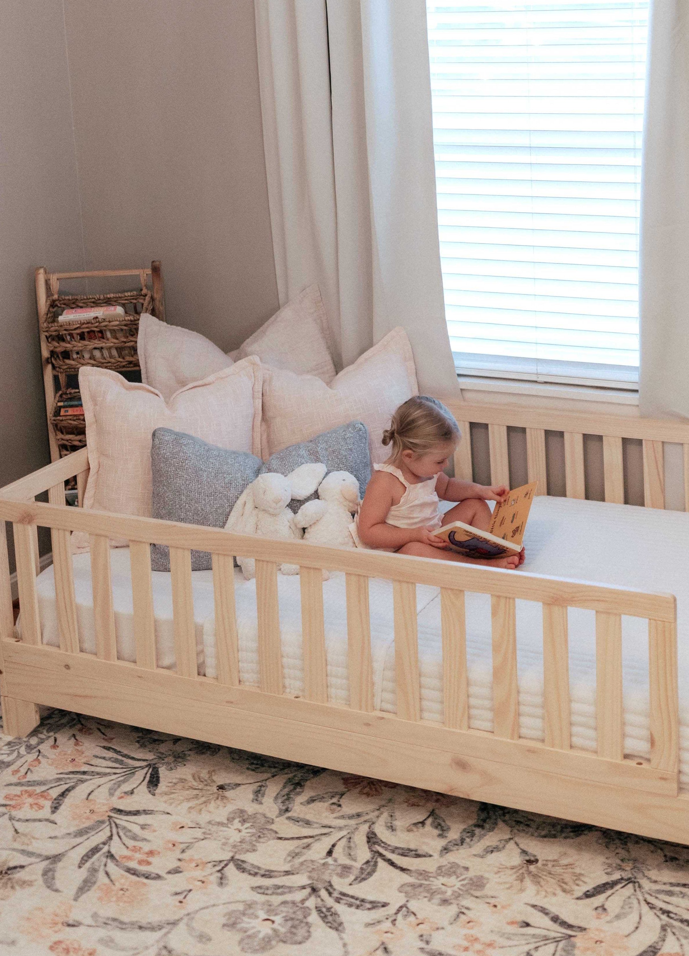 Luca Toddler Floor Bed with Rails in natural wood finish, shown in a cozy nursery with a child reading on the twin-size Montessori bed.