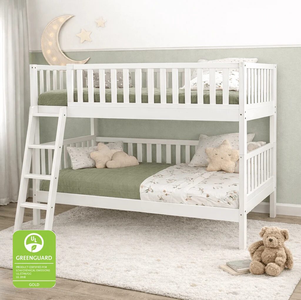 White wooden bunk bed with an attached ladder, styled with sage green bedding and decorative pillows in a nursery setting. A green GUARANTED GREENGUARD Gold badge is shown in the bottom-left corner.