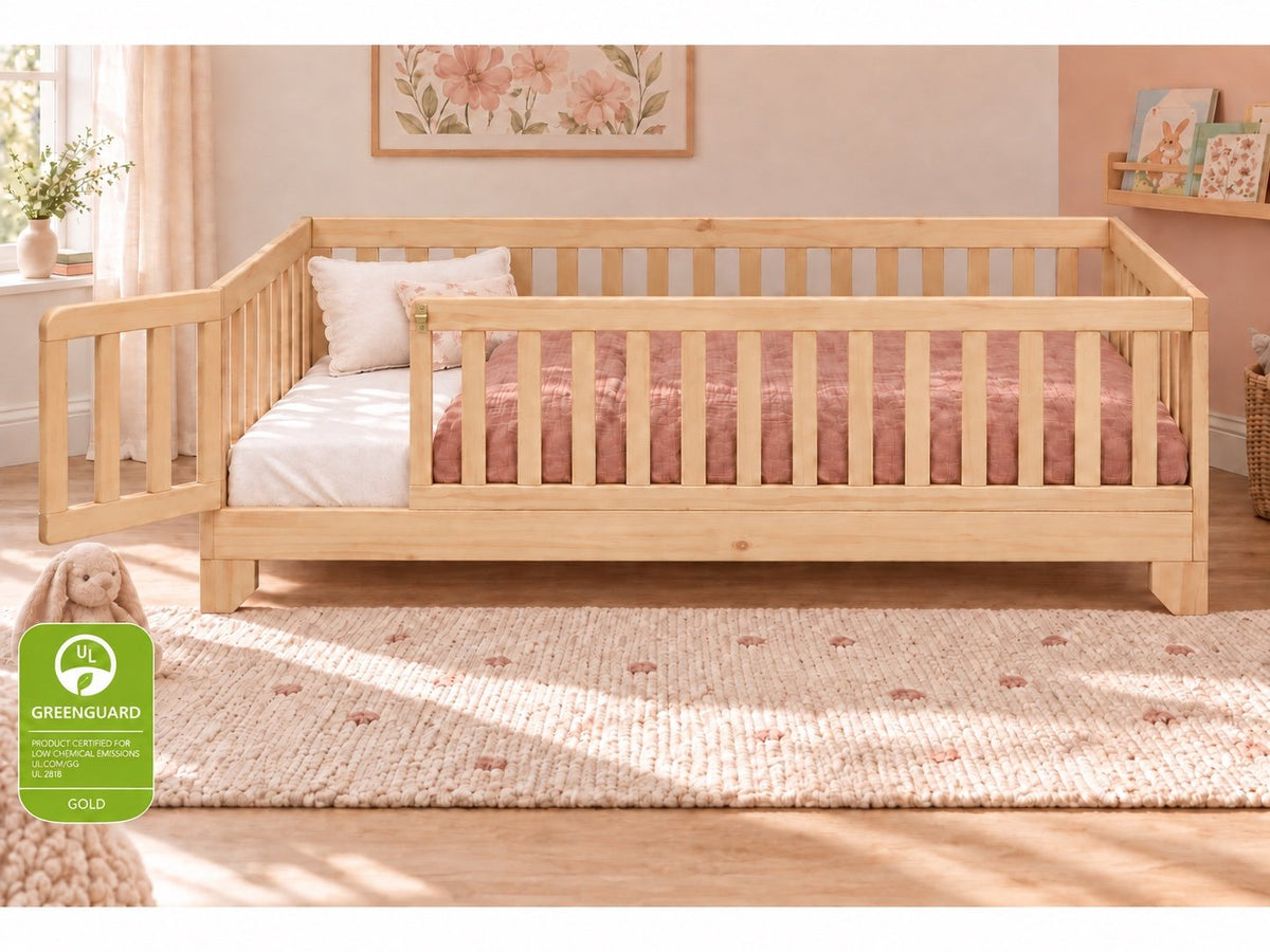 Luca Montessori twin size floor bed for toddlers with a natural finish, rails and a gate in a pink girls bedroom.